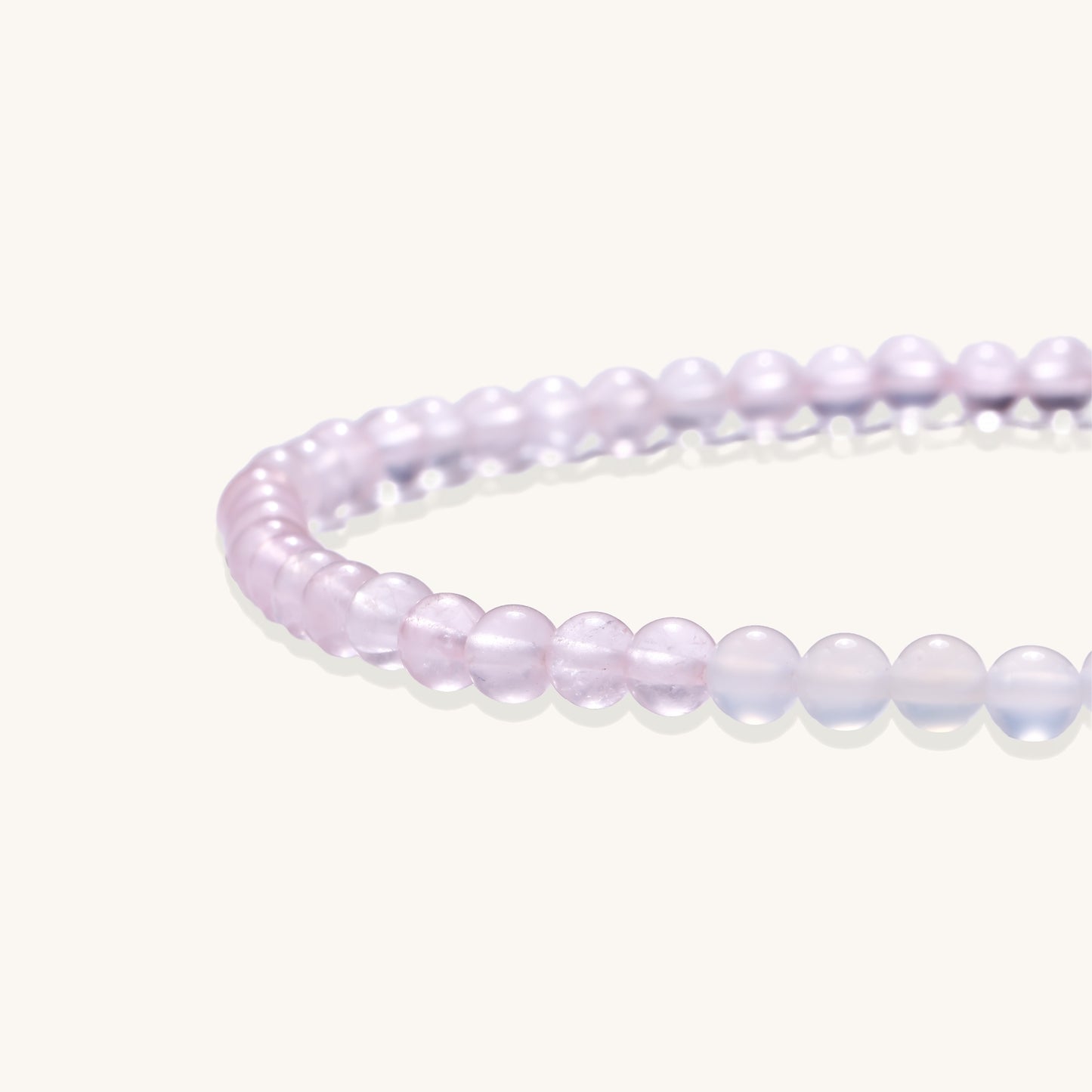 Stretchable bracelet with pink rose quartz and white agate beads, featuring a decorative tassel pendant on white background.