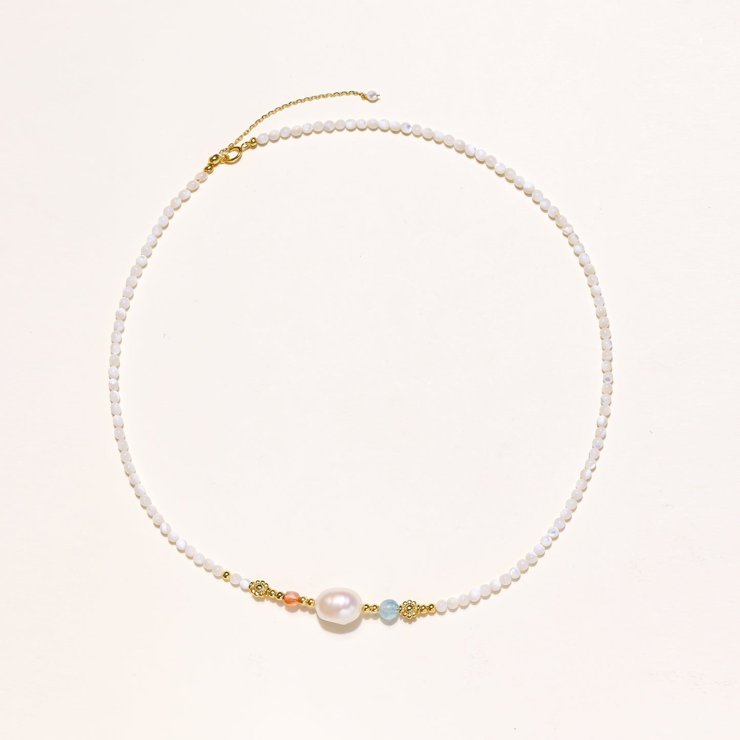 Delicate white beaded necklace with central freshwater pearl and gold-toned emerald accents on white background.