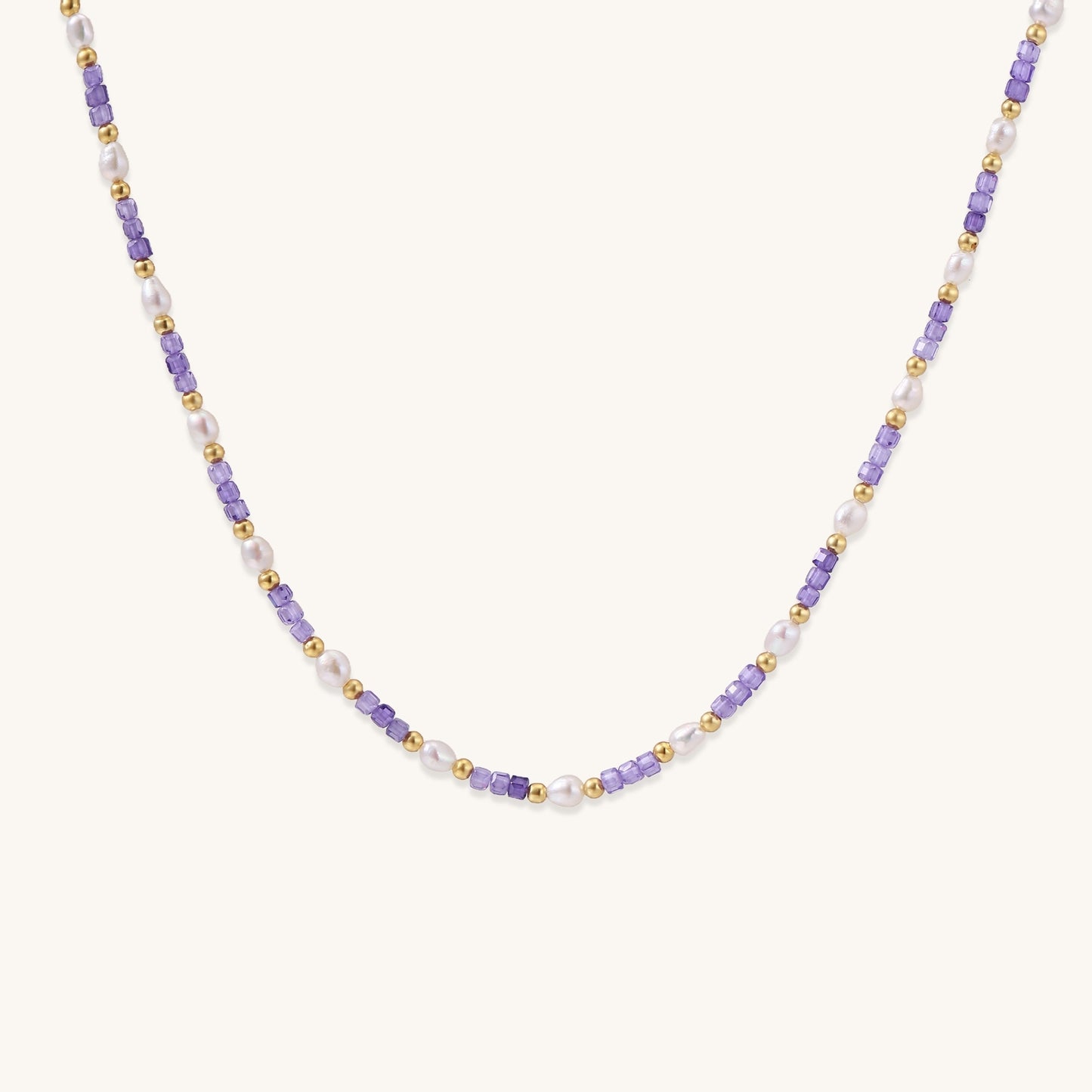 Delicate beaded necklace with alternating purple zirconia stones, white freshwater pearls, and gold-plated spacers on cream background.